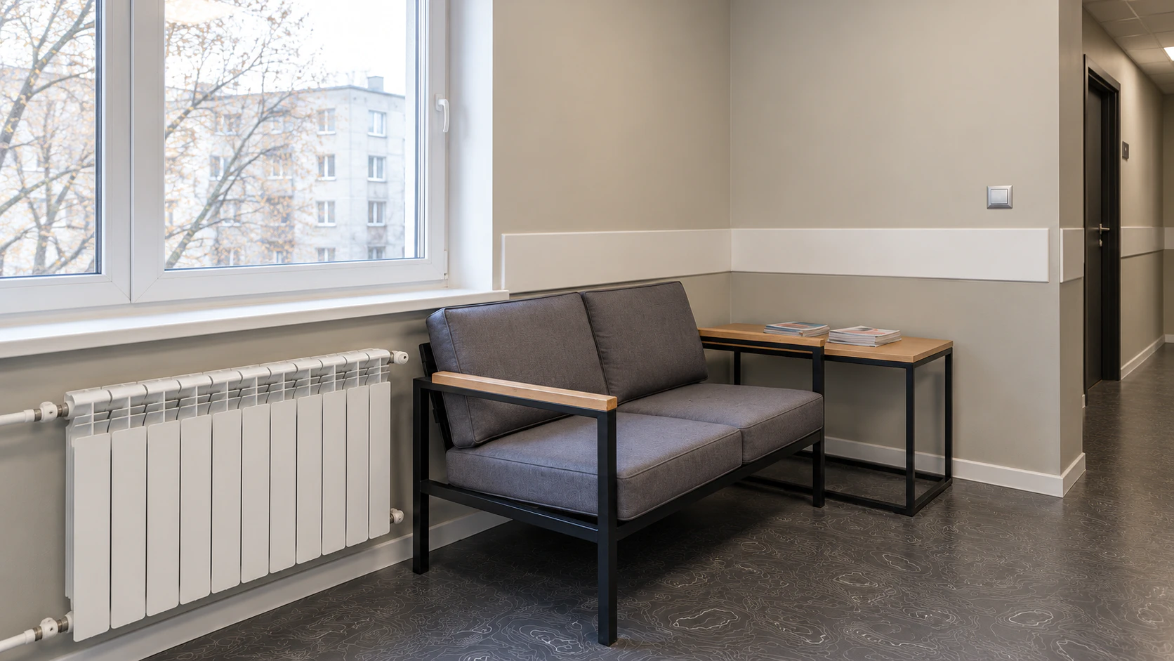 Зона ожидания с серым диваном и столиком у окна